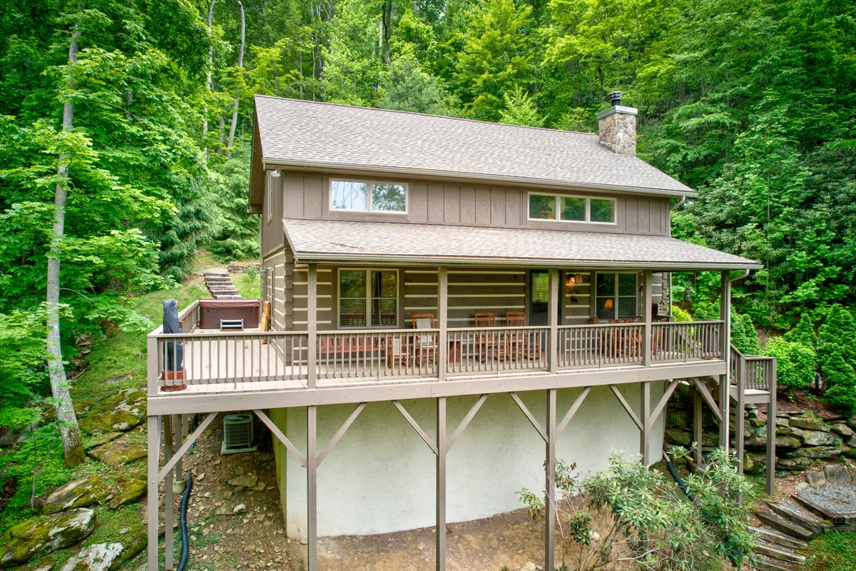 This exterior image shows a two-story wooden cabin surrounded by greenery, featuring a spacious deck with seating. The deck is clearly visible and appears to be securely enclosed, providing a sense of safety and relaxation for both people and pets.