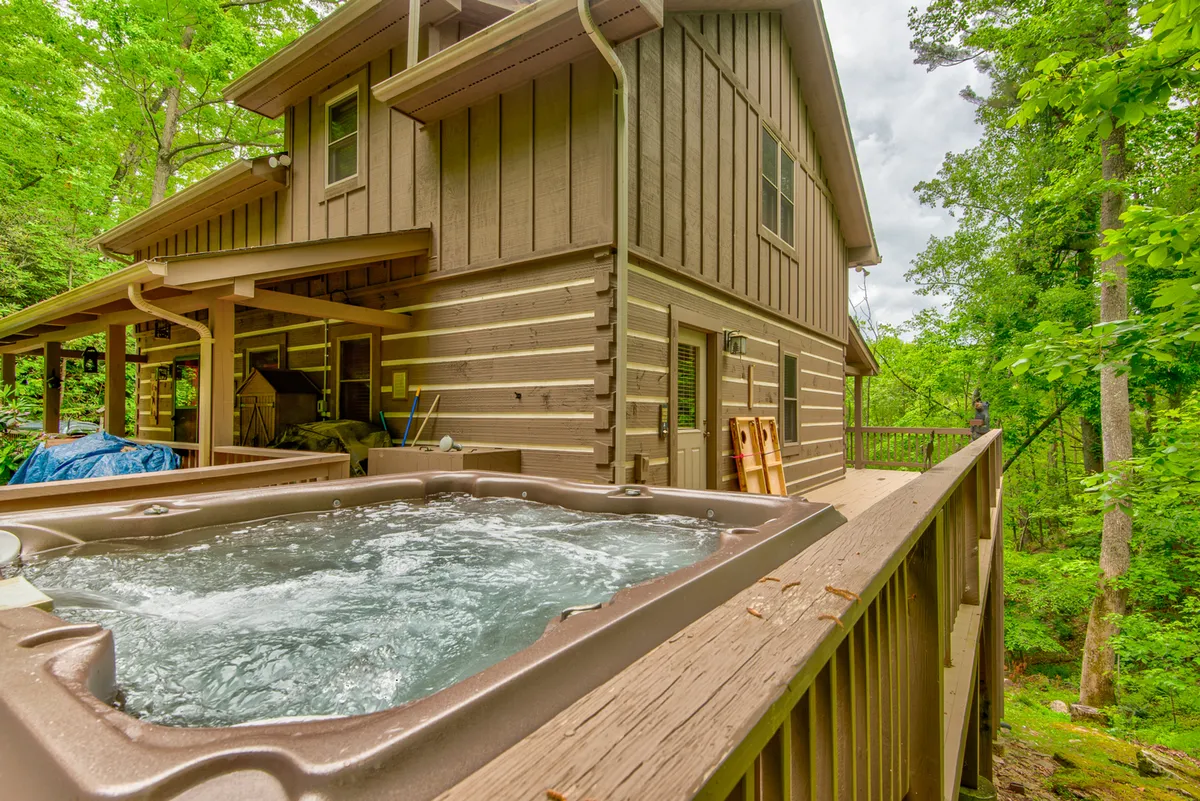 A wooden deck with a hot tub, surrounded by lush greenery and the log cabin's rustic architecture. The deck invites relaxation, enjoying nature, and appreciating mountain views—ideal for both soaking in the hot tub and savoring morning coffee or sunset toasts.