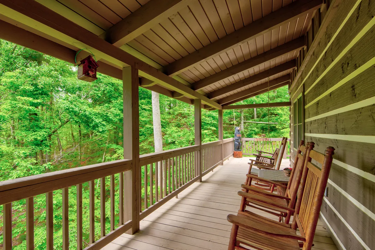 A peaceful porch overlooking greenery, complete with rocking chairs, a wooden railing, and a hanging lantern. The space feels calming and intimate, offering a direct connection to the surrounding natural beauty—an ideal setting for enjoying quiet moments or sharing a glass of wine at night.