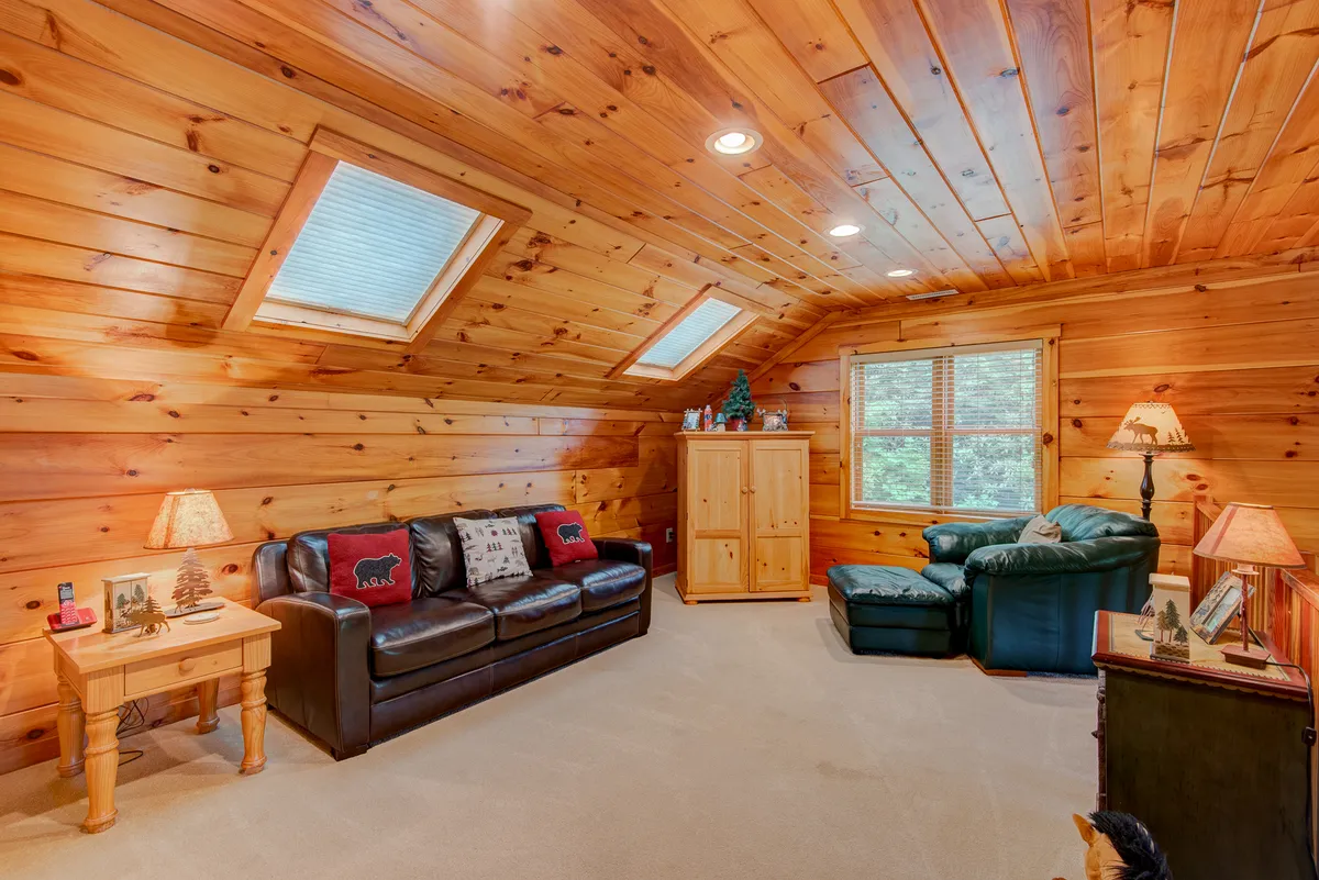 A versatile loft area featuring a comfortable sofa, coffee table, lamps, and large windows allowing plenty of daylight. The space is styled for both relaxation and independence, ideal for lounging, reading, or watching TV, and could easily accommodate a queen sleeper sofa as described.