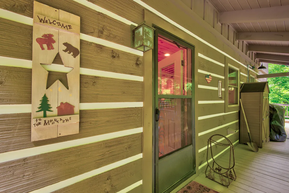 An inviting shot of the front entryway, featuring a welcome sign, front door, and decorative lanterns. The image highlights the main entrance to the cabin, suggesting a secure and welcoming arrival for guests and their dogs.