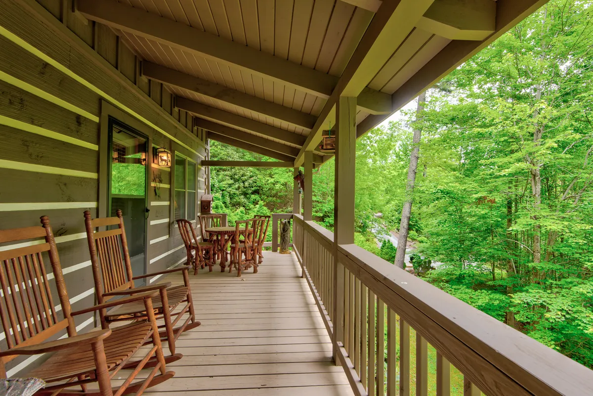 A cozy porch scene featuring classic wooden rocking chairs and a wooden table, surrounded by lush greenery. The inviting outdoor space radiates tranquility, with the greenery providing a private, natural backdrop ideal for relaxing, stargazing at night, or sharing intimate moments.